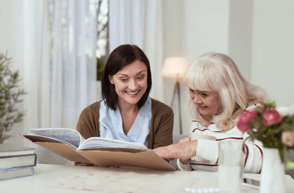 A senior parent and adult child happily flip through a family photo album.