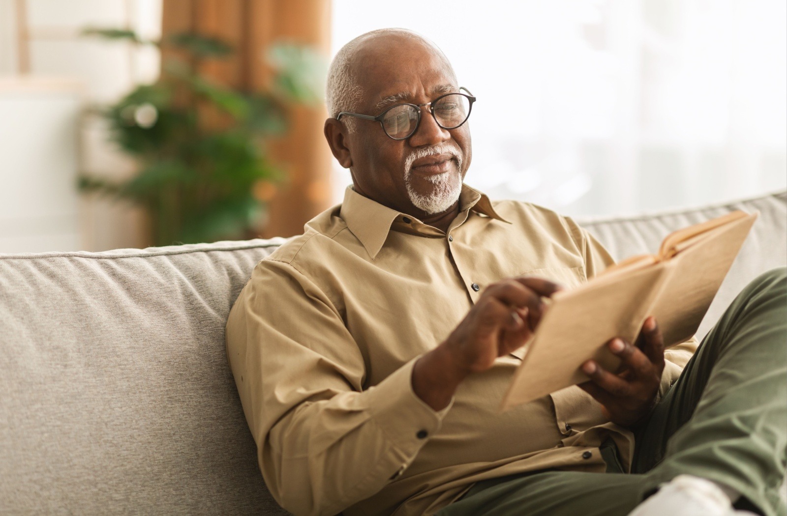 a senior sits on a couch reading a book