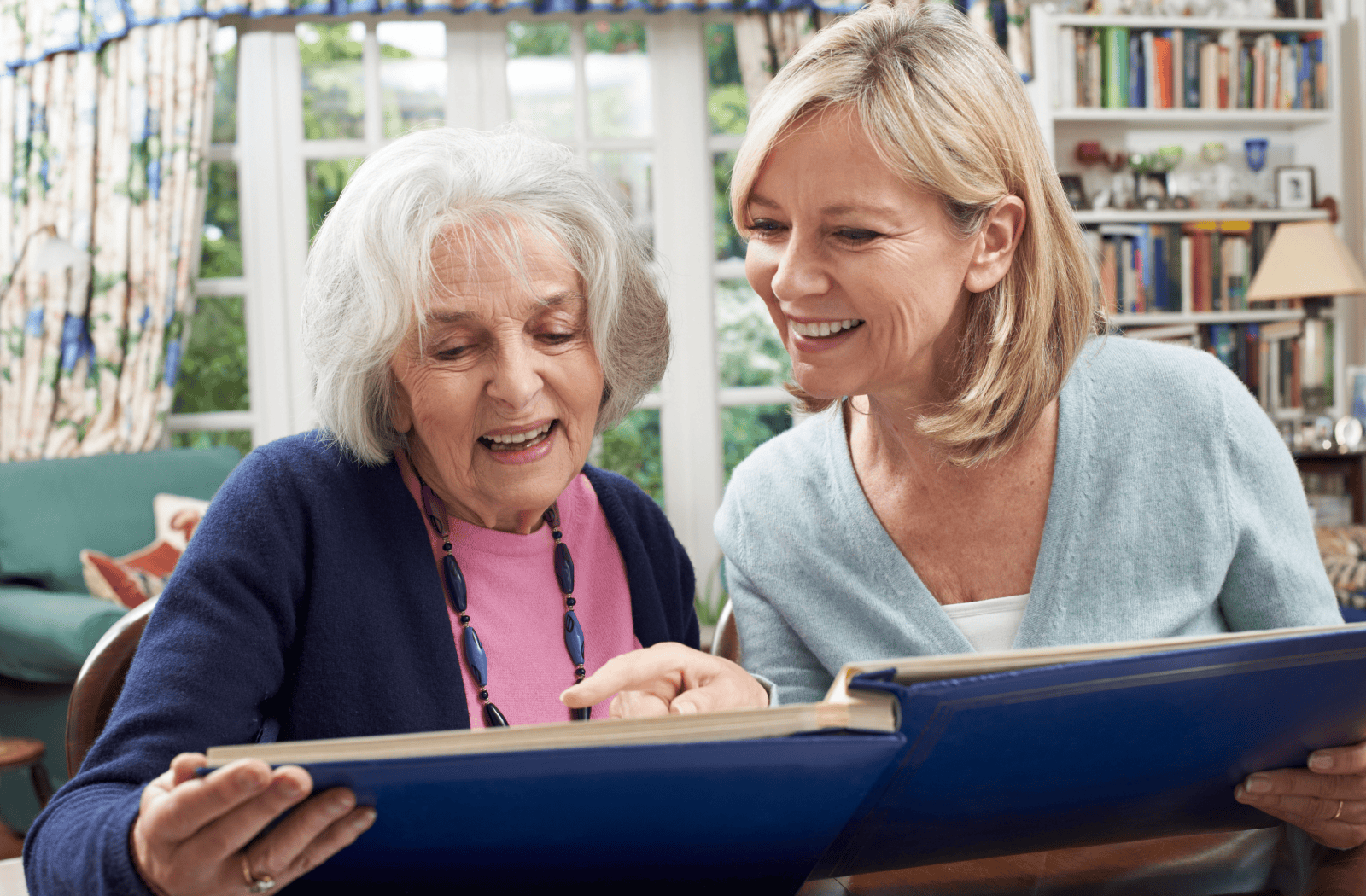 A senior and adult child browse happily through a family photo album.