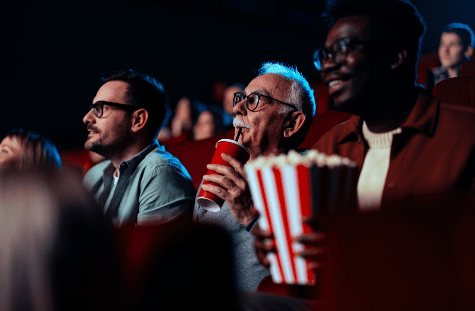 A senior sips a fountain drink in a crowded movie theatre.