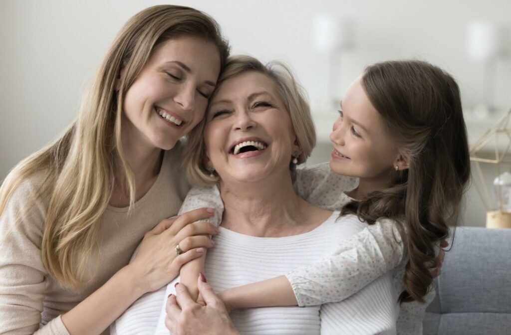 A multi-generational image of a senior, their adult child, and grandchild swapping happy stories.