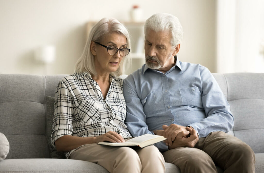 An older married couple sitting on the couch using a notebook as a memory aid.