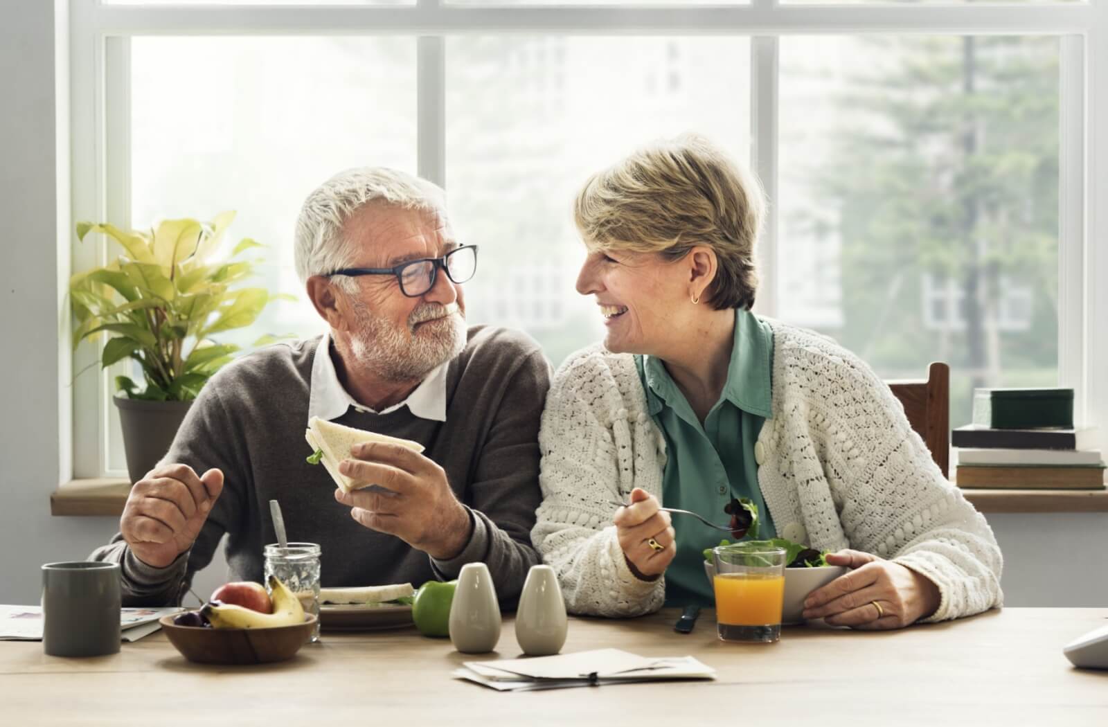 A pair of senior friends sitting side by side, happily enjoying a healthy meal together at a senior living community.