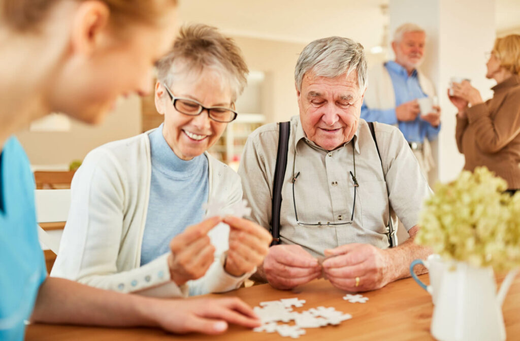 A group of older adults in memory care work together to assemble a white puzzle while laughing