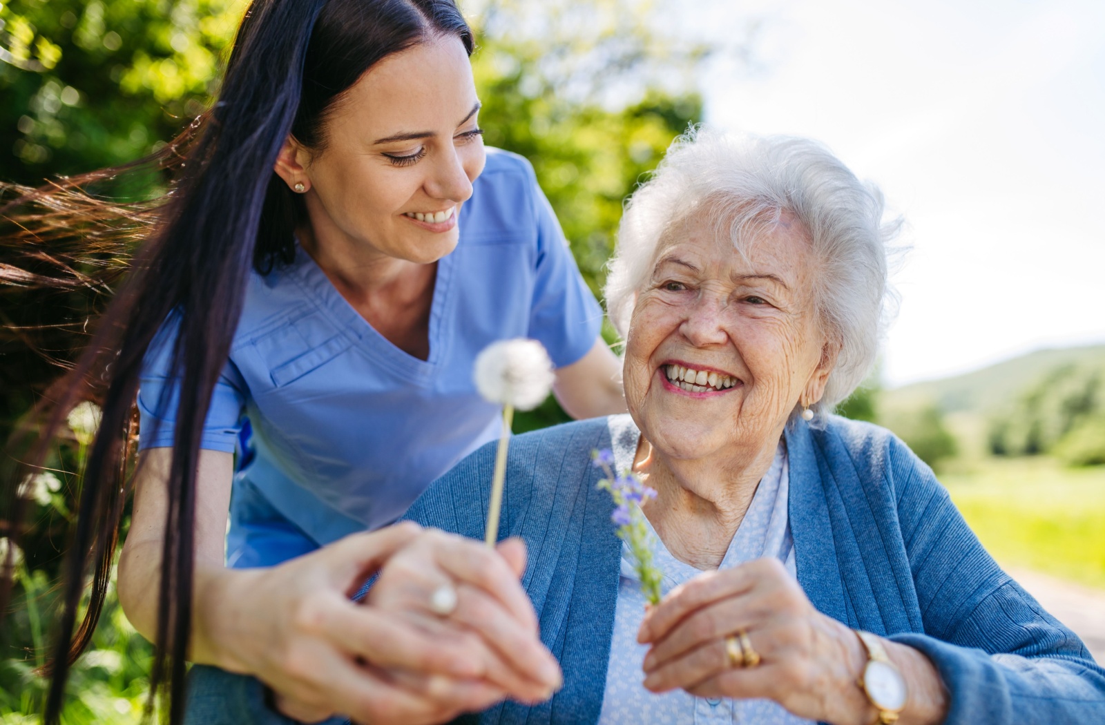 : A woman in a memory care community and a staff member looking at flowers outside together.