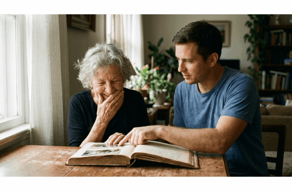 An older adult and a younger person smiling while looking through a photo album together at a table.